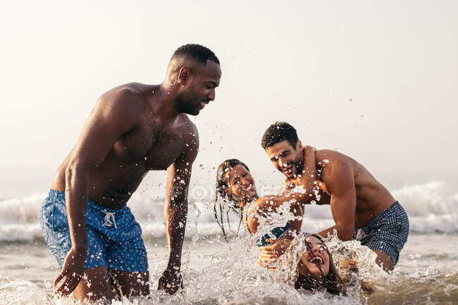 Група різних друзів у плавальному вбранні розважаються у хвилястому морі, а ввечері насолоджуються літнім днем. — стокове фото