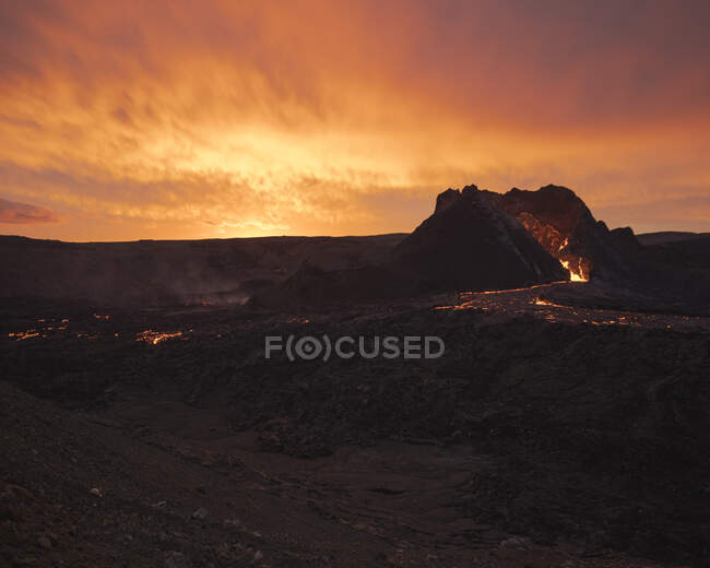 Vue pittoresque du volcan actif avec lave chaude situé contre un ciel nuageux au coucher du soleil en Islande — Photo de stock