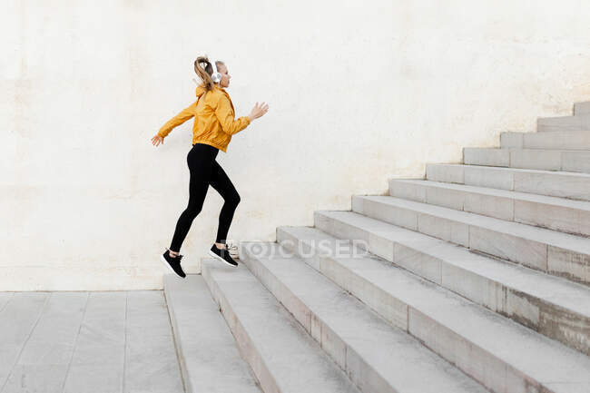 Jeune femme caucasienne sportive portant un casque et une tenue de sport, courant sur les escaliers à l'extérieur — Photo de stock