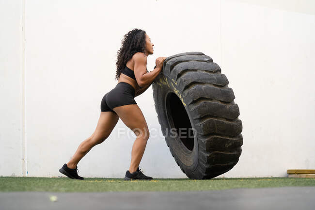 Вид сбоку на мускулистую азиатскую спортсменку, прокатывающую тяжелую шину во время интенсивных тренировок — стоковое фото