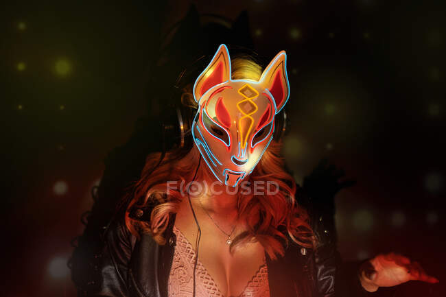 Анонимная женщина в маске креативной лисы с неоновыми орнаментами, работающая во время вечеринки в ночном клубе — стоковое фото