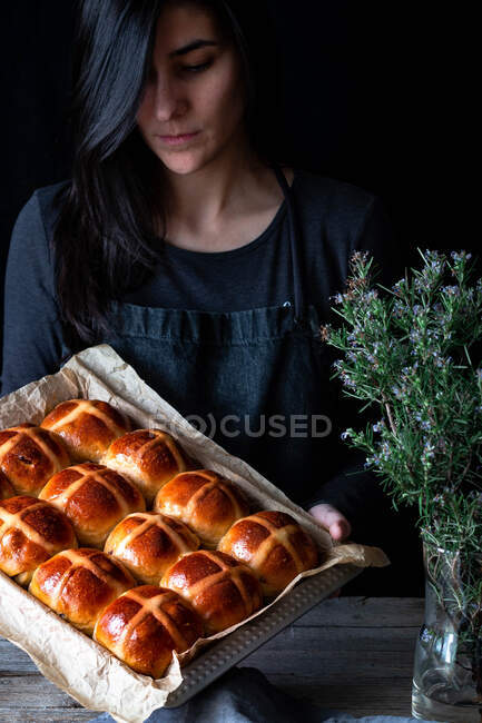 Female baker holding puff freshly baked hot cross buns on baking tray — Stock Photo