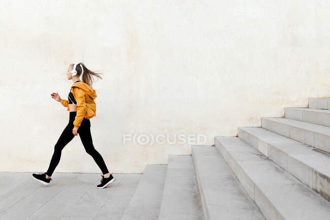 Joven atlética mujer caucásica con auriculares y ropa deportiva, corriendo en las escaleras al aire libre - foto de stock