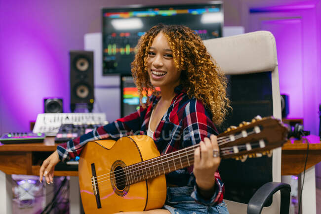 Giovane chitarrista afroamericana femminile con chitarra classica seduta in studio mentre guarda la fotocamera — Foto stock