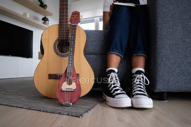 Неузнаваемая афроамериканка-музыкантка сидит на диване рядом с акустической гитарой и мандолиной — стоковое фото