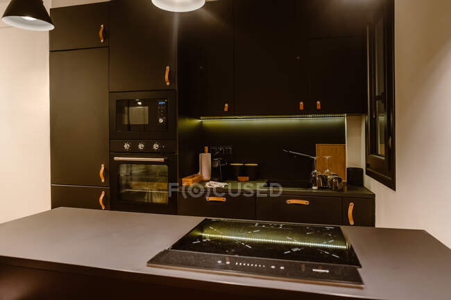Інтер'єр кухні з лампами, що світяться над лічильником з електричною плитою з піччю і мікрохвильовою піччю — стокове фото