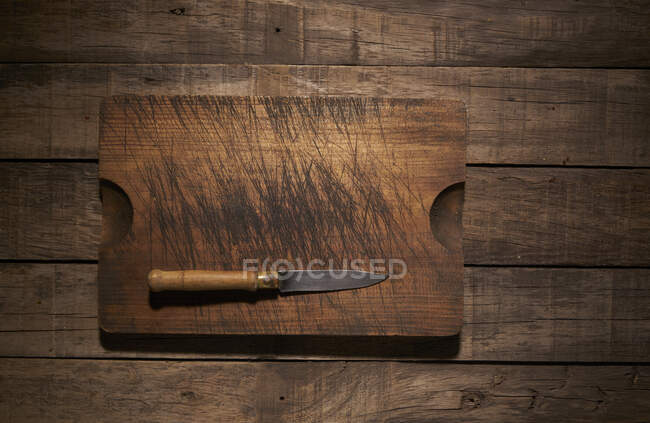 Top view composition with sharp kitchen knife and weathered wooden cutting board placed on rustic plank table — Stock Photo
