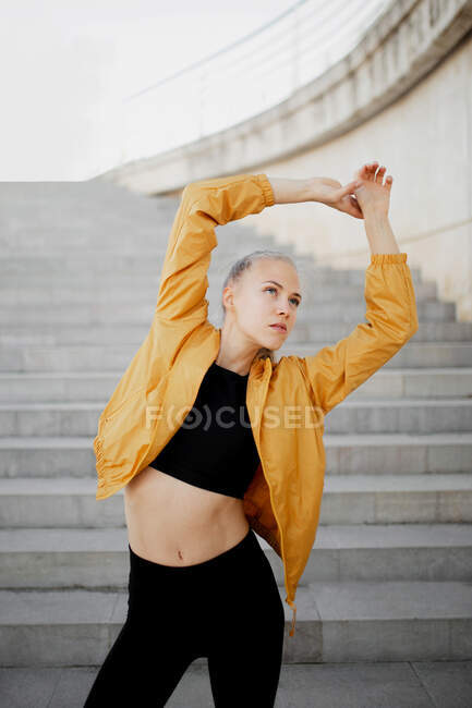 Молодая атлетичная белая женщина, растянувшаяся на улице возле лестницы — стоковое фото