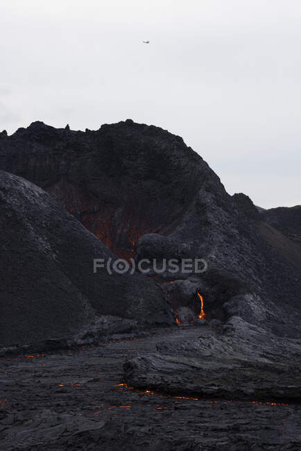 Blick auf den Strom heißer orangefarbener Lava, der am Morgen durch bergiges Gelände in Island fließt — Stockfoto