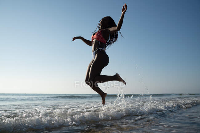 Mulher negra com tranças na praia pulando na praia — Fotografia de Stock