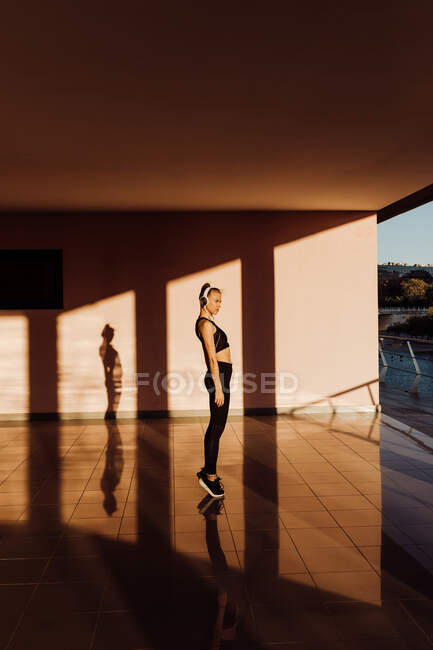 Jeune femme caucasienne athlétique travaillant au coucher du soleil, ombres et lumière sur le fond — Photo de stock
