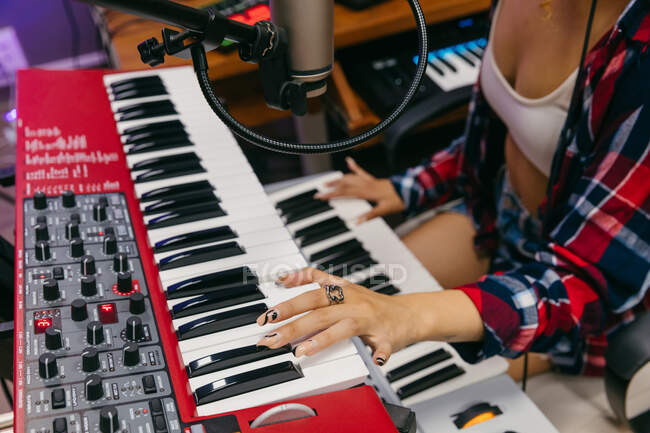 Cortado cantor feminino afro-americano irreconhecível em fone de ouvido tocando sintetizador enquanto executando música em microfone em estúdio de gravação — Fotografia de Stock