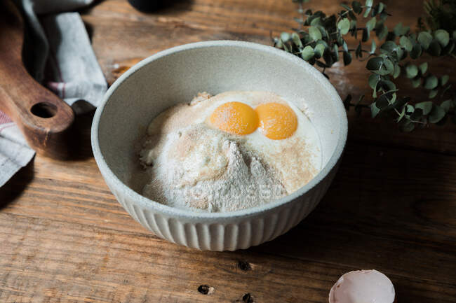 Dall'alto ciotola con uova e panna mescolate con pangrattato e farina sul tavolo di legno durante la preparazione della pasticceria — Foto stock