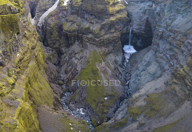 Do córrego acima da água limpa que cai de penhascos pedregosos ásperos cobertos do musgo no campo de Islândia — Fotografia de Stock