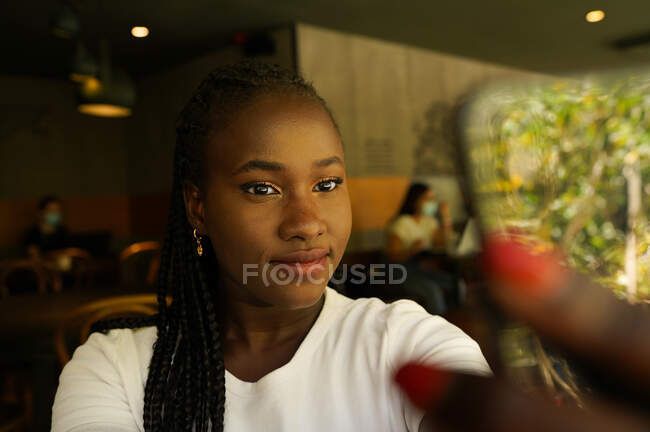 Charmante Afroamerikanerin mit Zöpfen, die im Café Selbstaufnahmen macht und lächelt — Stockfoto