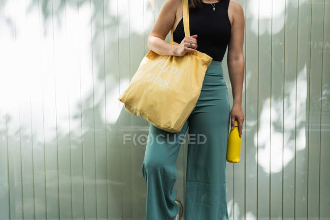 Mujer anónima satisfecha de pie con bolsa de compras ecológica en la calle en verano y mirando hacia otro lado - foto de stock