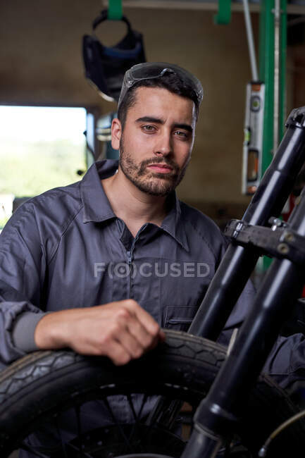 Hombre trabajador de garaje en la tapa sentado en el banco de trabajo - foto de stock