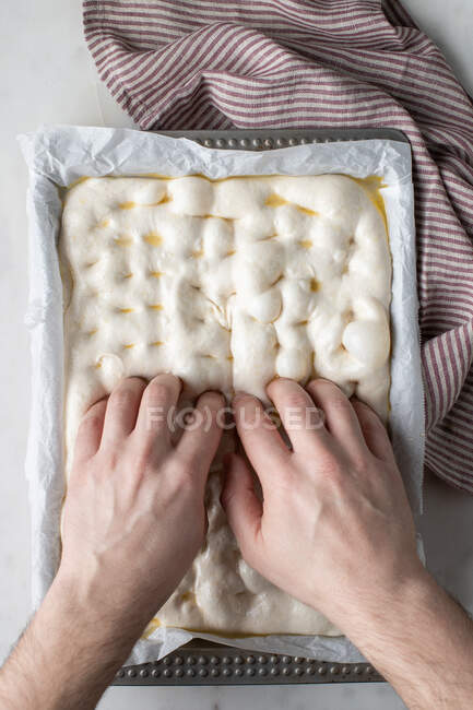 Top view of faceless person preparing raw dough for bread placed on baking paper on table — Stock Photo