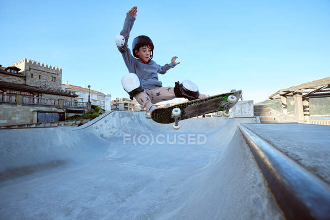 Adolescente niño en casco protector monopatín en el parque de skate en el día soleado en la orilla del mar - foto de stock