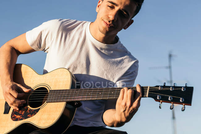 Young man sitting playing acoustic guitar on a rooftop — Stock Photo