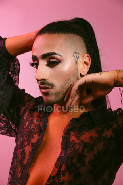 Retrato de mujer barbuda transgénero glamorosa en maquillaje sofisticado posando mirando hacia otro lado sobre fondo rosa en el estudio - foto de stock