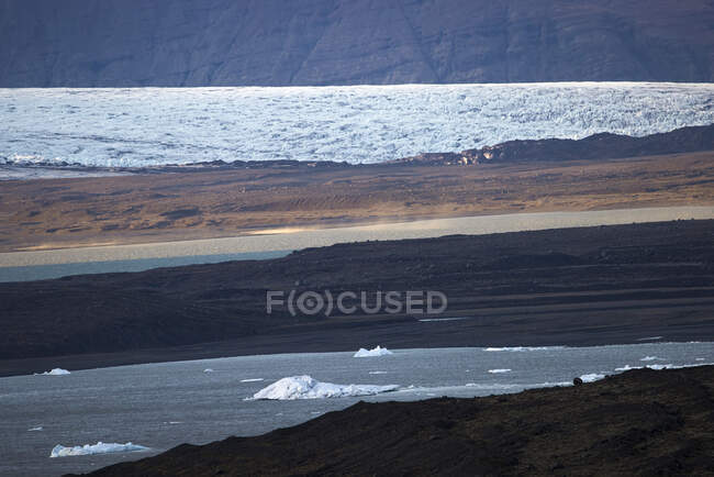 Ghiacci galleggianti sull'acqua del fiume vicino alle coste grezze nella giornata primaverile in Islanda — Foto stock