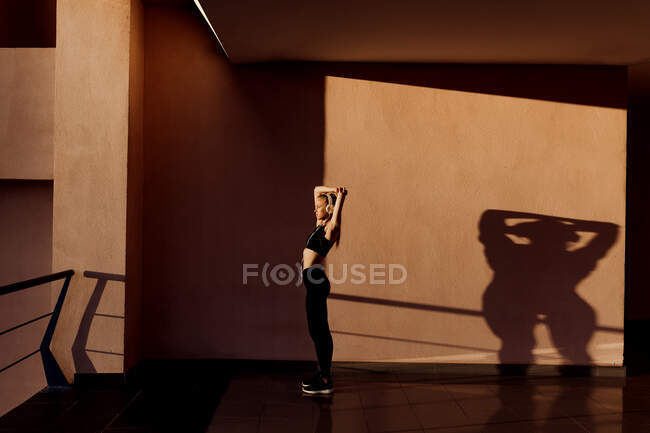 Молода атлетична жінка, яка слухає музику і розтягується на заході сонця, тіні та світло на задньому плані. — стокове фото