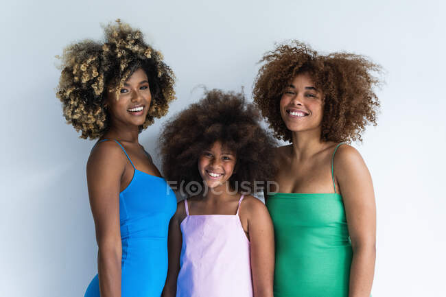Encantada madre afroamericana e hijas con peinado afro de pie sobre fondo blanco en el estudio y mirando a la cámara - foto de stock