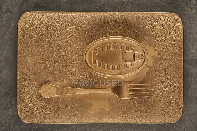 Top view of gold fork placed near sealed canned food on rectangular copper tray — Stock Photo