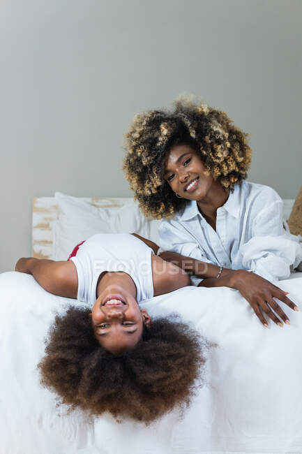 Positivo afroamericano madre e figlia con i capelli ricci sorridenti alla fotocamera mentre si rilassa sul letto e divertirsi — Foto stock