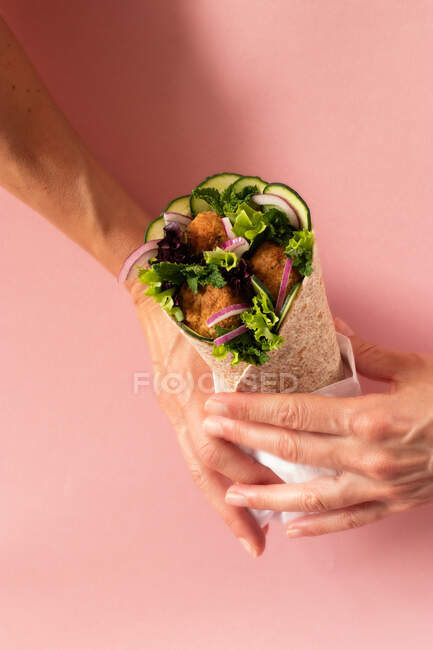 Recadré mains personne méconnaissable tenant enveloppement falafel végétalien sur fond rose coloré — Photo de stock