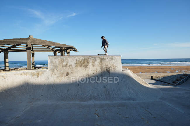 Unrecognizable teen boy in protective helmet riding skateboard in skate park on sunny day on seashore — Stock Photo