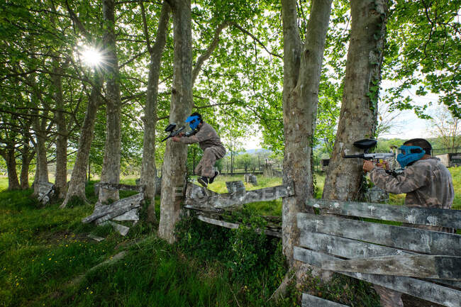 Équipe méconnaissable de joueurs masculins armés et vêtus de vêtements de camouflage jouant au paintball dans les bois en été — Photo de stock