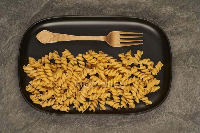 Ansicht der Goldgabel in der Nähe von ungekochten Fusilli-Nudeln auf Tablett auf dem Tisch — Stockfoto