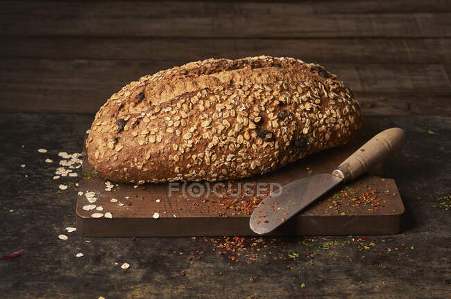 Зверху апетитний хрусткий домашній хліб з вівсяними пластівцями та родзинками, розміщеними з ножем на дерев'яній обробній дошці — стокове фото