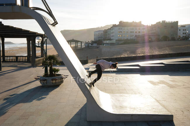 Side view of unrecognizable male skater riding down rescue tower located on seashore in summer — Stock Photo