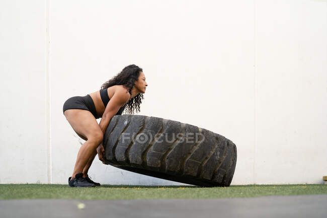 Seitenansicht einer muskulösen asiatischen Athletin, die während des intensiven Trainings schwere Reifen umkippt — Stockfoto