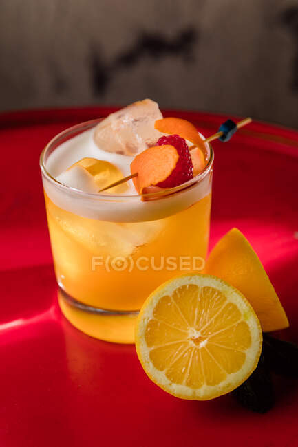 Verre en cristal d'Amaretto Cocktail aigre garni de zeste d'orange et de framboise servi avec un citron coupé en deux — Photo de stock
