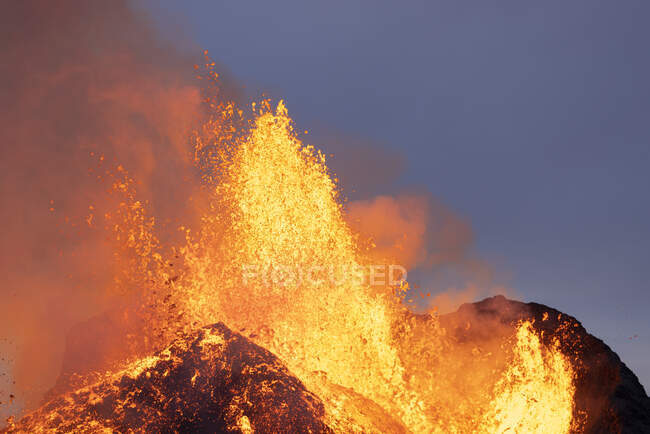 Спалахи гарячої оранжевої лави вивергаються з вулканічної вершини в оточенні диму в Ісландії. — стокове фото