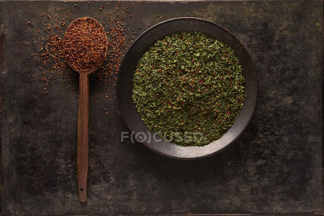 Composizione aerea con cucchiaio con pomodori secchi al sole macinati posizionati vicino alla ciotola con spezie vegetali verdi su fondo nero — Foto stock