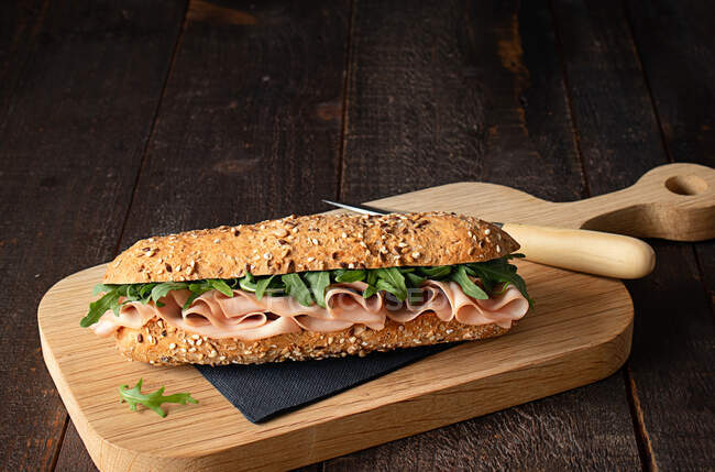 Sandwich à la mortadelle avec feuilles de fusée sur fond de table en bois foncé — Photo de stock
