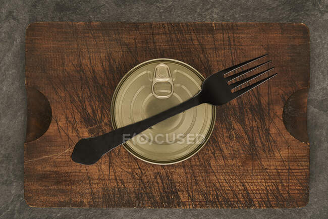 De cima arranhado tábua de corte com garfo e lata selada com alimentos preservados em mesa rústica madeira — Fotografia de Stock