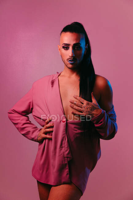 Ritratto di donna barbuta transgender glamour in sofisticato make up posa con le mani in vita contro sfondo rosa in studio guardando la fotocamera — Foto stock
