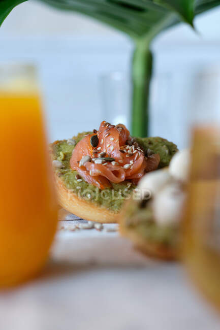 Bicchieri di succo di frutta e tisana serviti sul tavolo di legno con toast di avocado sano assortiti con formaggio e salmone durante la colazione nel caffè all'aperto — Foto stock