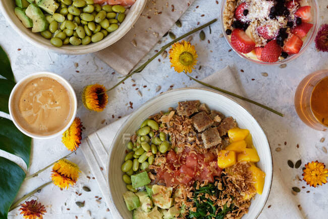 Appetitlich sortierte Poke-Schalen mit Avocado-Toasts und Säften auf dem Tisch serviert mit Beerendessert in der Nähe verstreuter frischer Blumen — Stockfoto