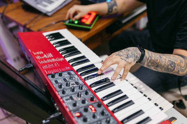 Crop unrecognizable tattooed male pianist playing modern synthesizer while composing music at desk in recording studio — Stock Photo