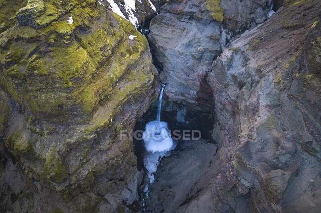 Сверху поток чистой воды падает с грубых каменных скал, покрытых мхом в сельской местности Исландии — стоковое фото