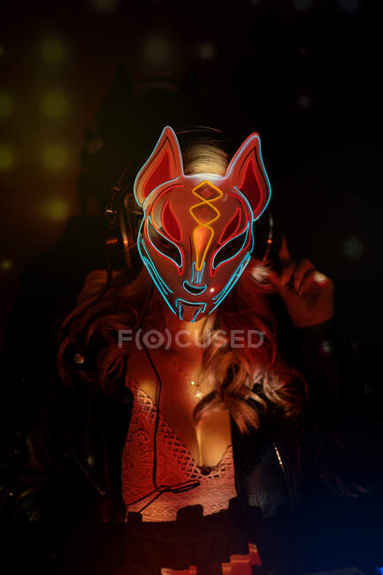 Mulher anônima em máscara de raposa criativa com ornamentos de néon trabalhando durante a festa em boate — Fotografia de Stock
