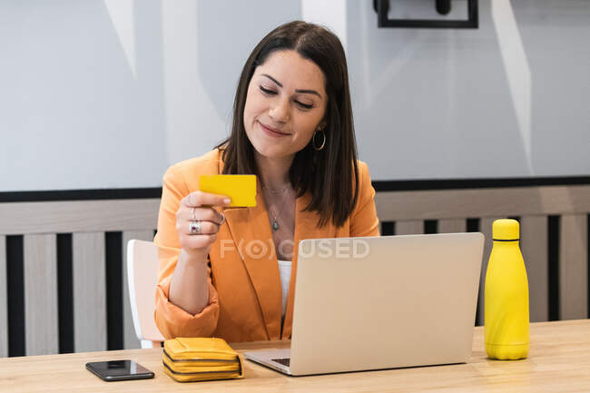Femme gaie utilisant une carte en plastique et payer pour les achats lors des achats en ligne via un ordinateur portable — Photo de stock