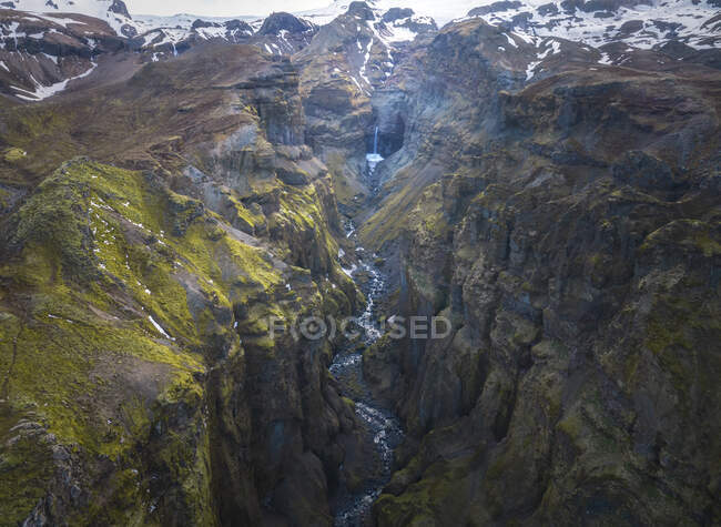 De haut ruisseau d'eau propre tombant des falaises pierreuses rugueuses couvertes de mousse dans la campagne d'Islande — Photo de stock